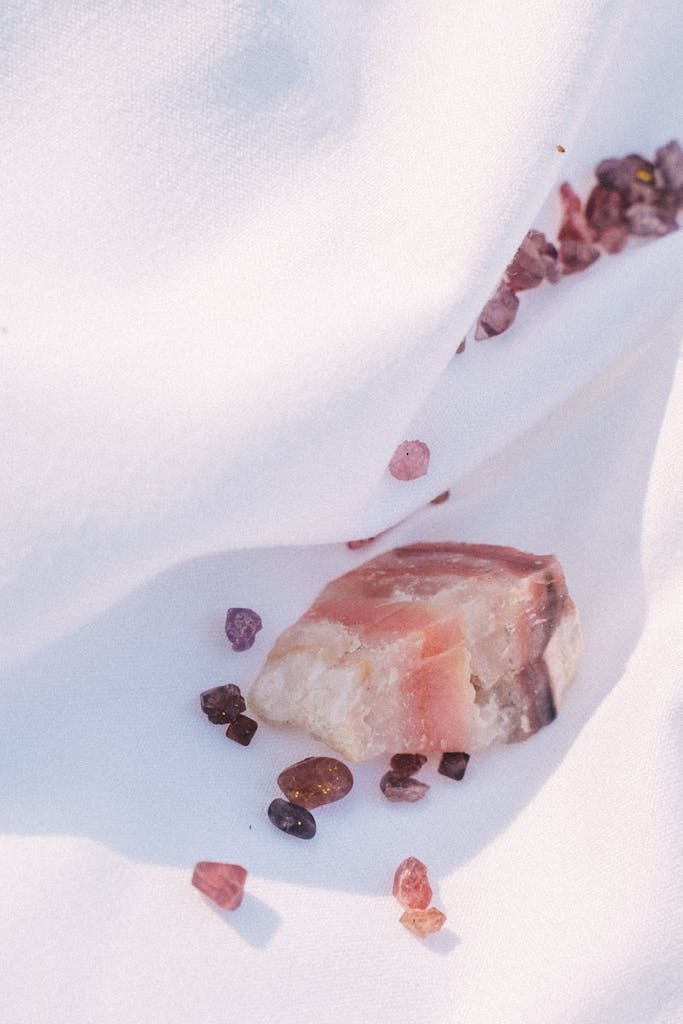 A close-up of rose quartz and garnet gemstones on a white textured surface.