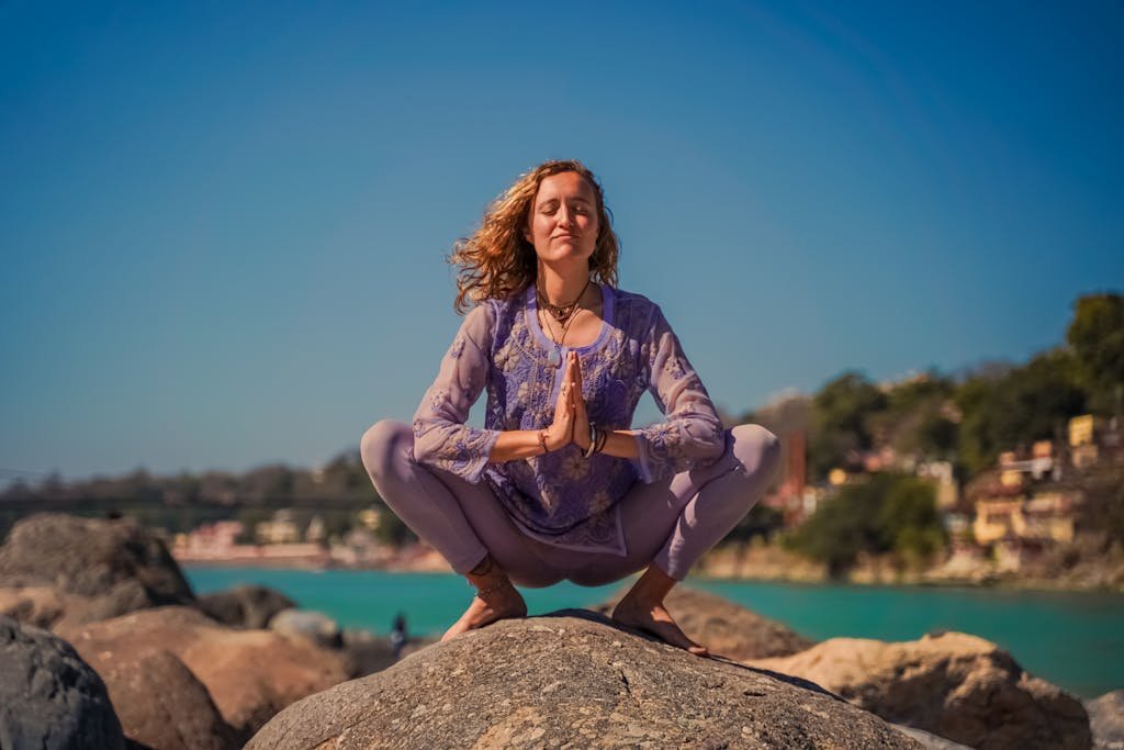 A woman practicing yoga on rocks in Rishikesh with a serene backdrop.