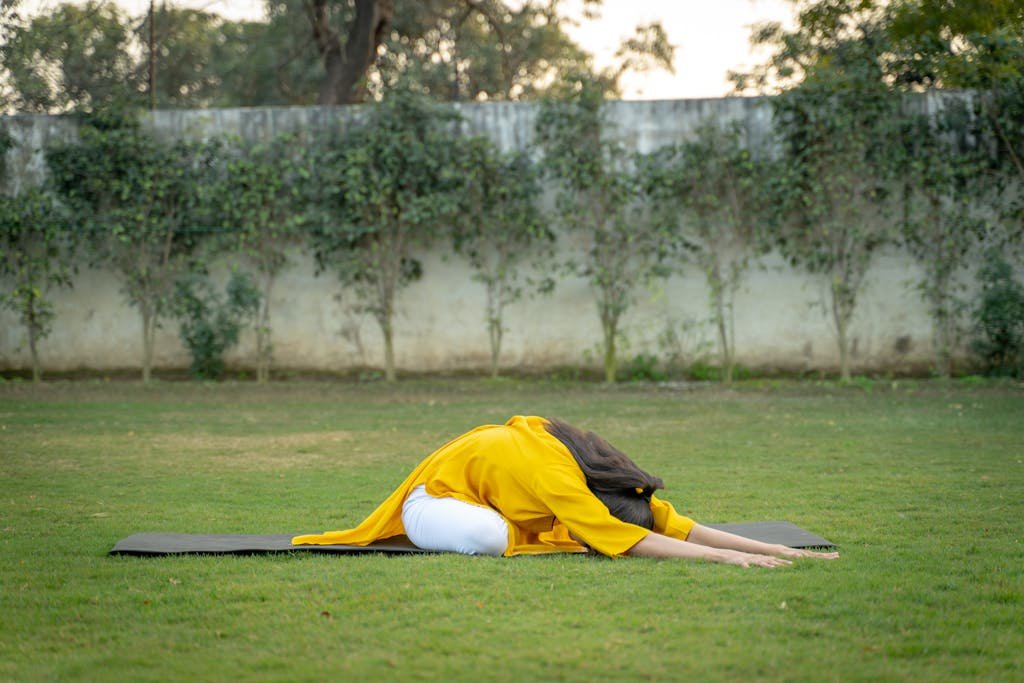 Adult woman performing yoga pose outdoors on a mat surrounded by green grass and trees.