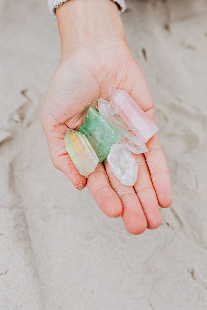 Close-up of a person's hand holding colorful gemstones on a sandy beach shoreline.