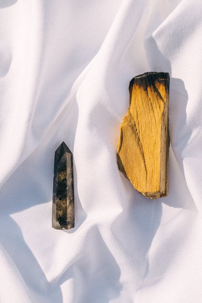 Elegant display of a healing crystal and palo santo on white silk fabric, creating a serene vibe.
