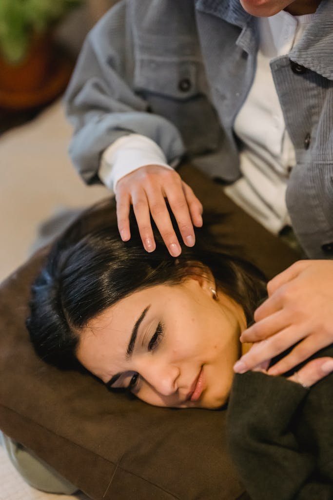 From above of young worried ethnic female with dark hair lying on knees of crop unrecognizable friend at home