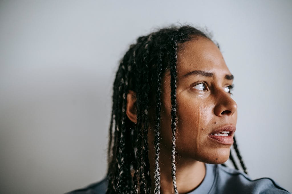 Grieved depressed African American female with dreadlocks crying hopelessly and looking away in dismay against white wall