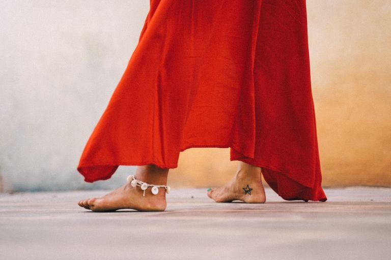 Close-up of a woman dancing barefoot in a flowing red dress with anklet outdoors.