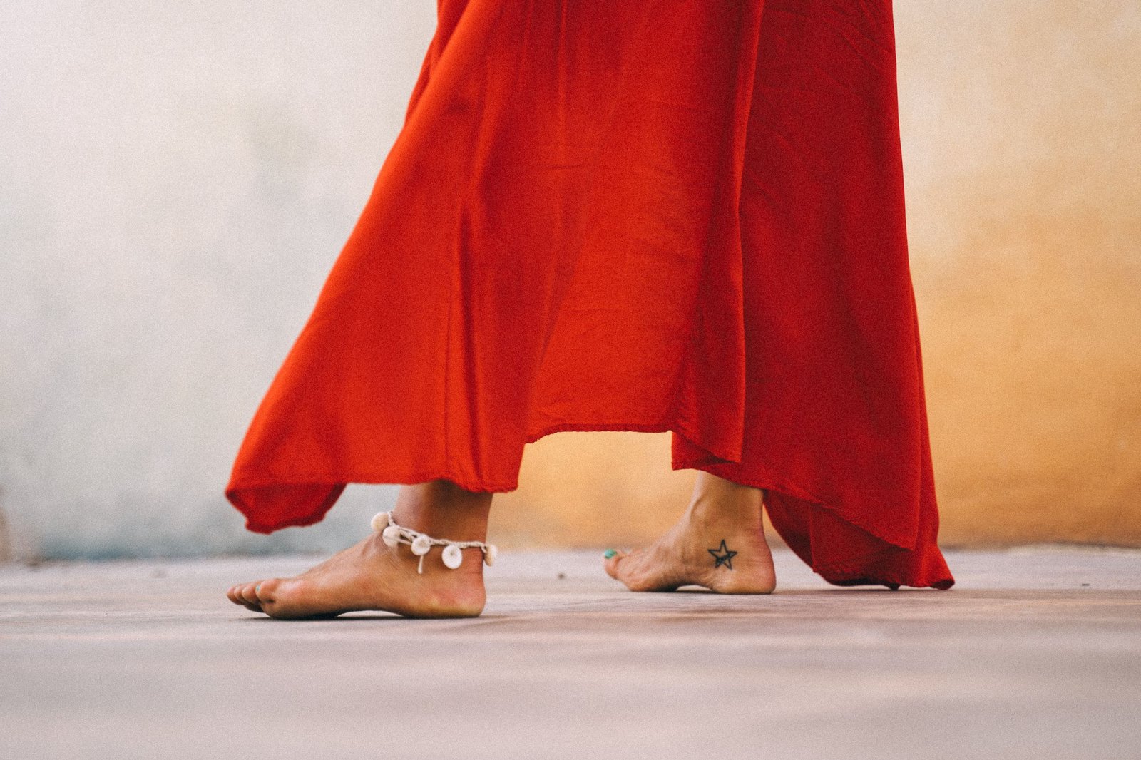 Close-up of a woman dancing barefoot in a flowing red dress with anklet outdoors.