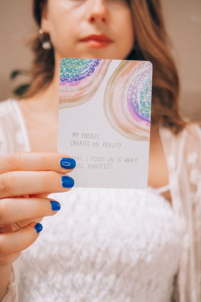 Close-up of a woman holding an oracle card with an inspirational message and vivid colors.